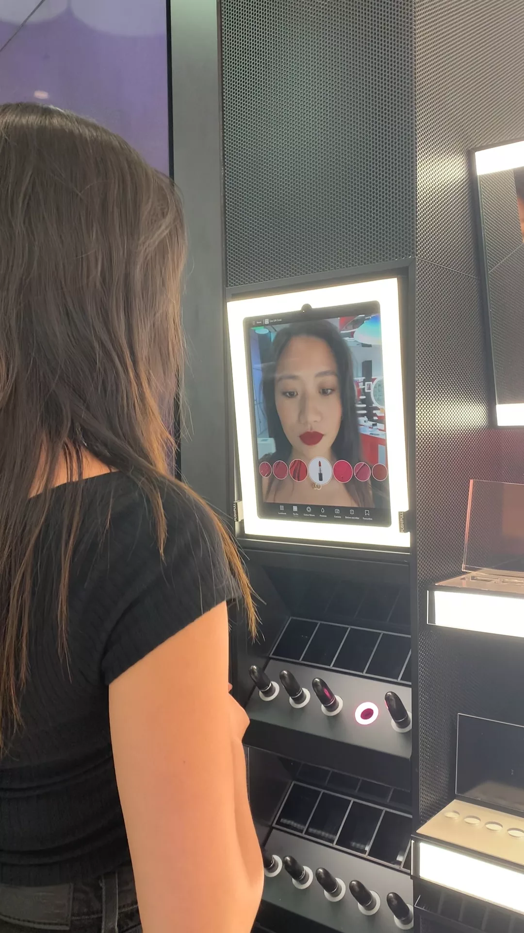 A woman seeing the lipstick that she picked up off a lipstick stand being rendered on her face as an augmented reality effect on an iPad.