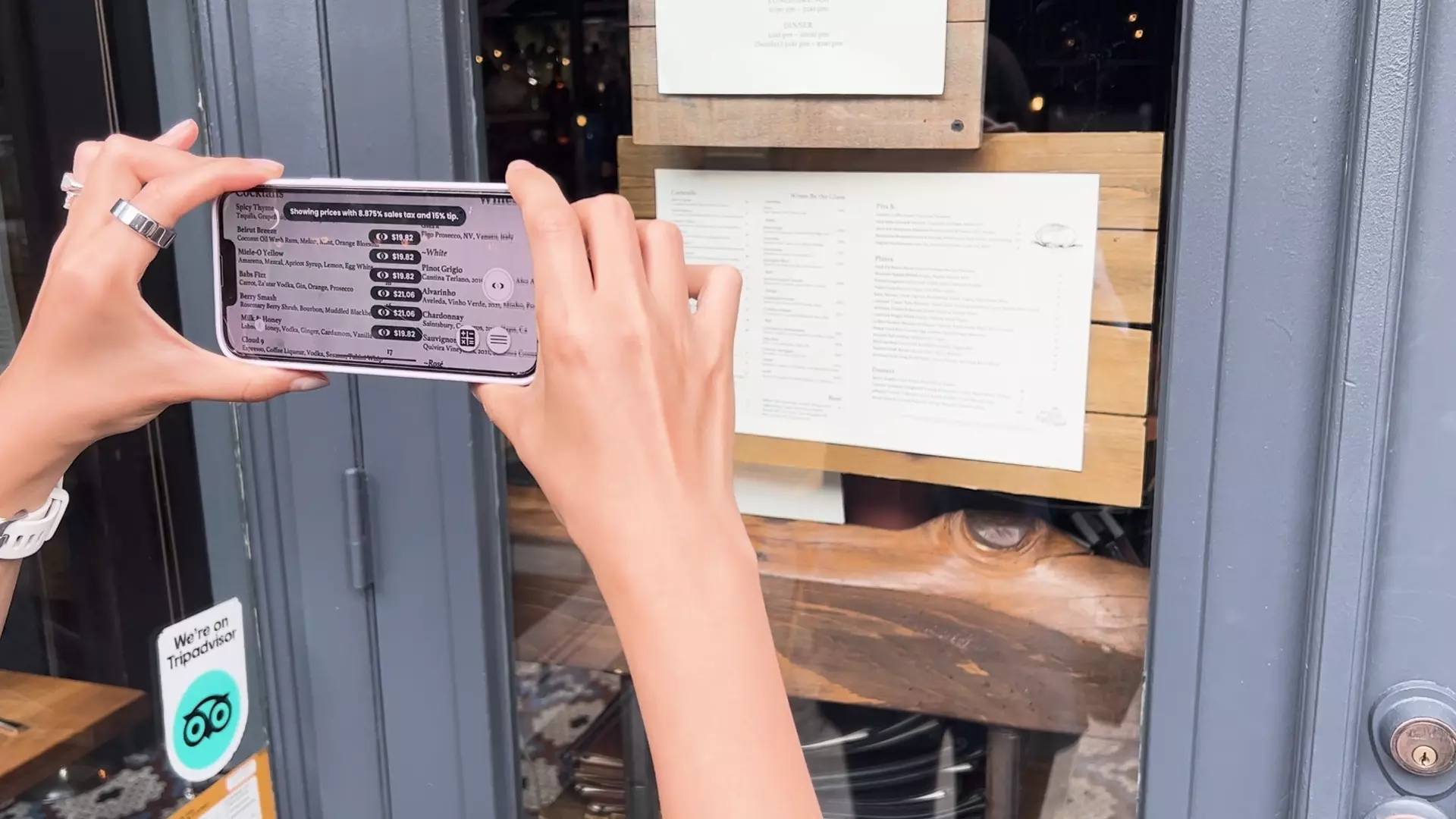 A woman holding an iPhone that is using the Price After app. The Price After camera is pointed at a restaurant menu and on the phone prices can be shown next to the menu prices that show the prices of the food and drink after tip and tax.