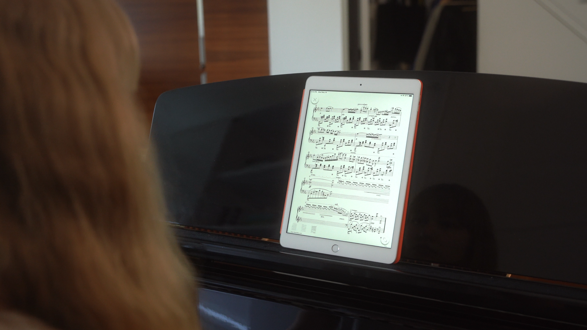 <p>A woman in front of a piano looking at an iPad.</p>