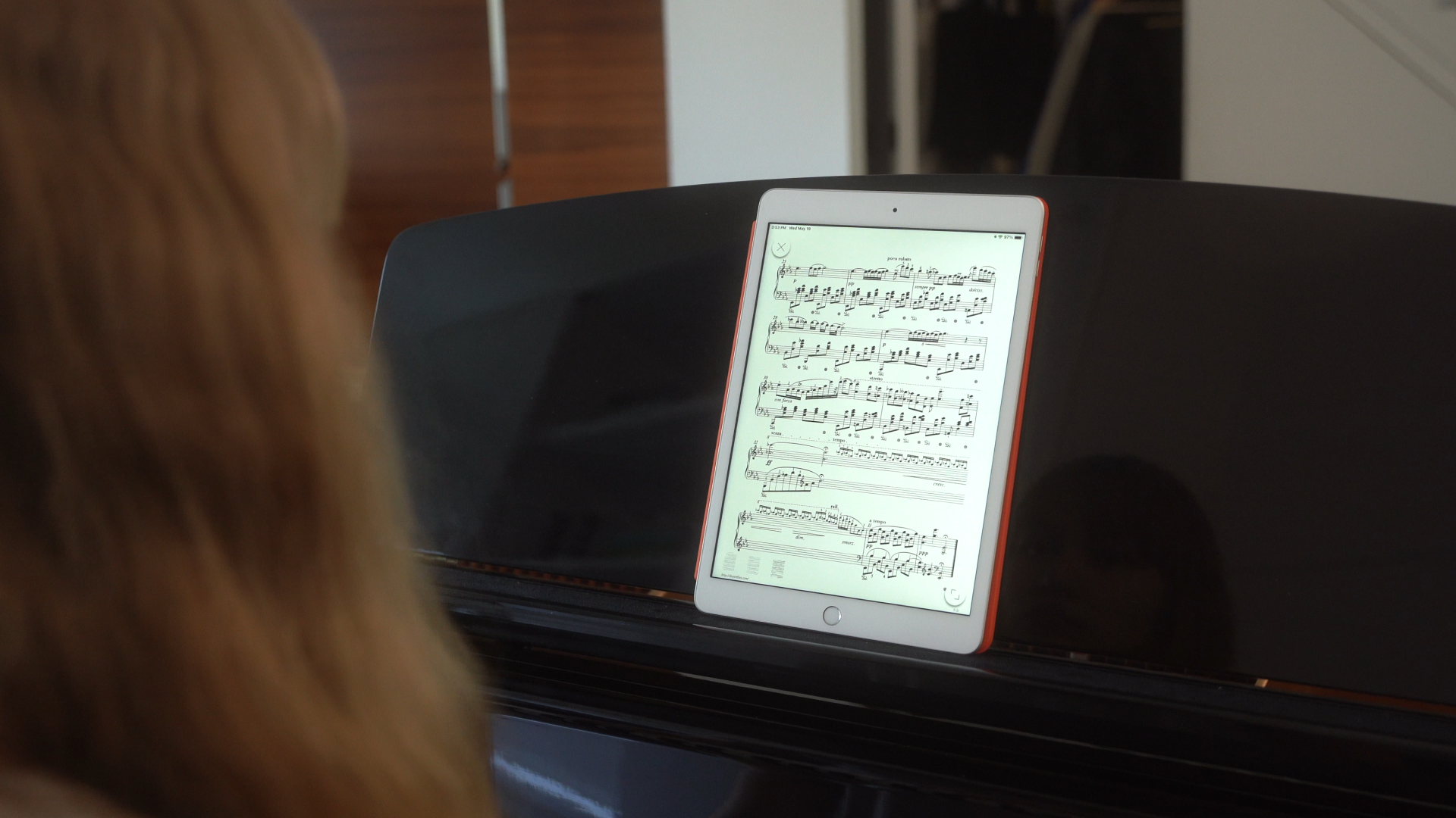 A woman in front of a piano looking at an iPad.