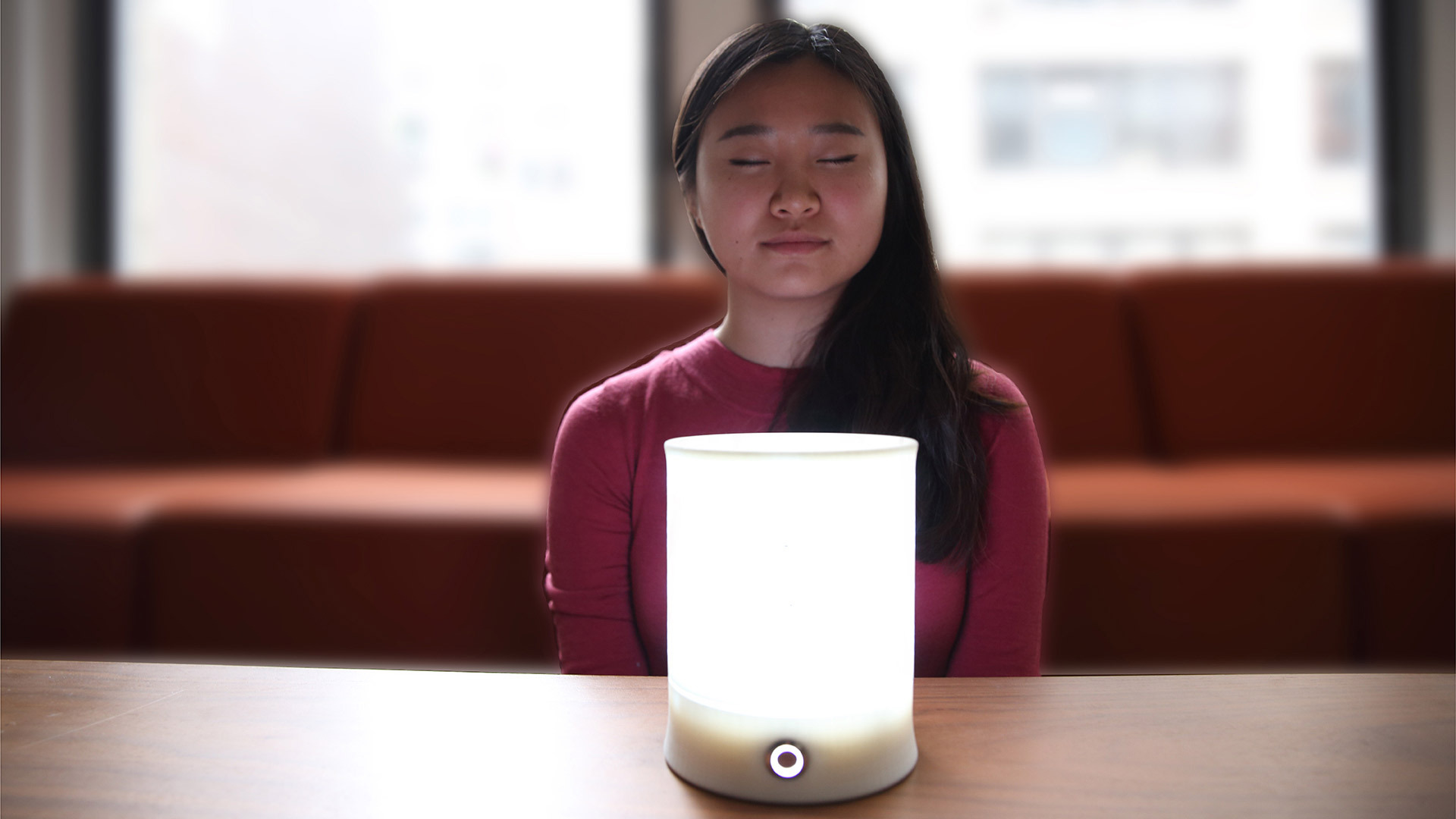 A woman meditating before Lumo - the smaller Solace lamp intended for customer use.